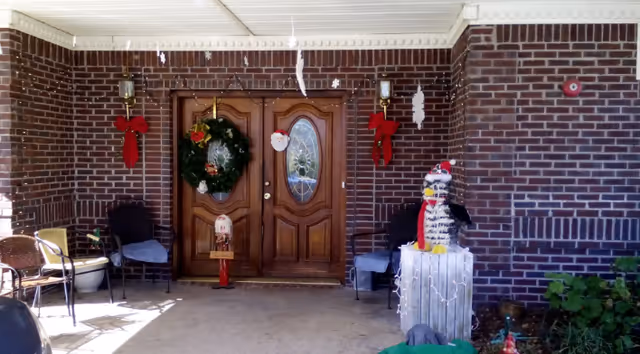 Covered brick entrance with double wooden doors decorated for Christmas, a wreath on the door and a penguin holiday decoration on the porch.