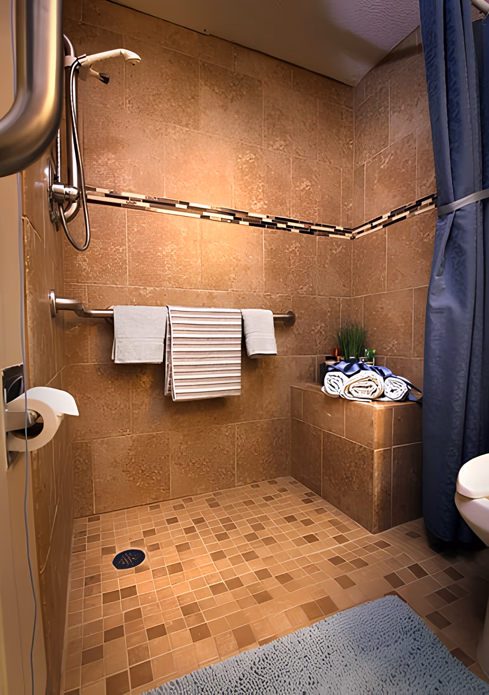Tiled walk-in shower with a handheld showerhead, grab bar, built-in bench topped with folded towels and a shower curtain.