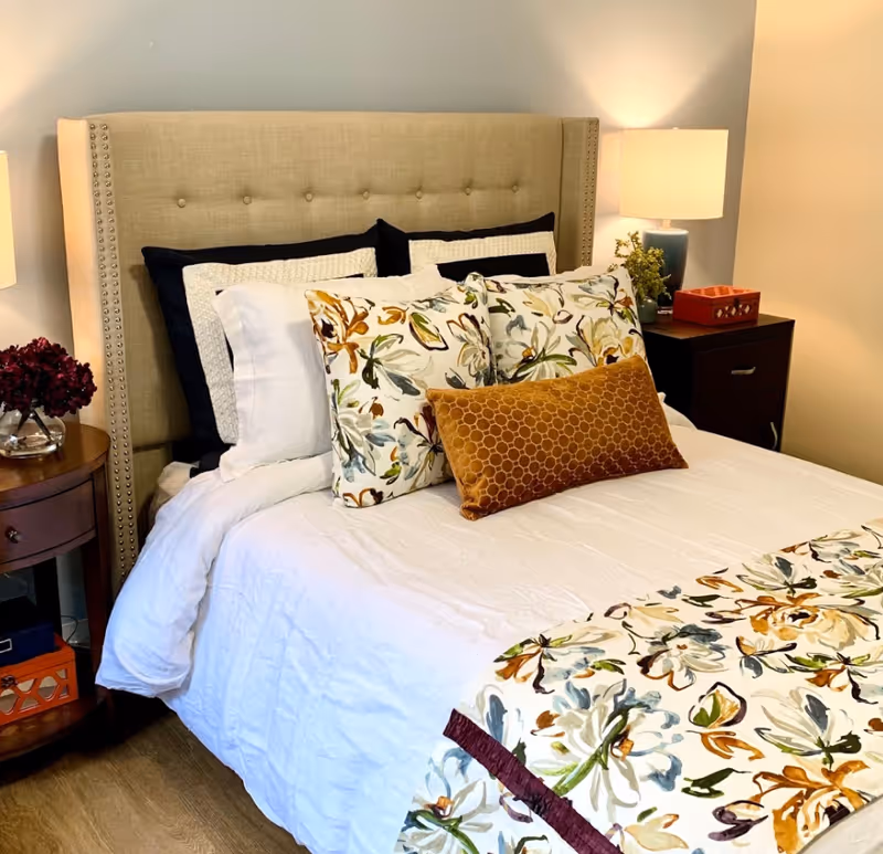 A neatly made bed with a beige tufted headboard, floral pillows and bedside tables with lamps in a bedroom.