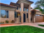 Front exterior view of a modern single-story house with a tiled roof, large windows, a double garage, and a well-maintained green lawn with palm trees and shrubs.