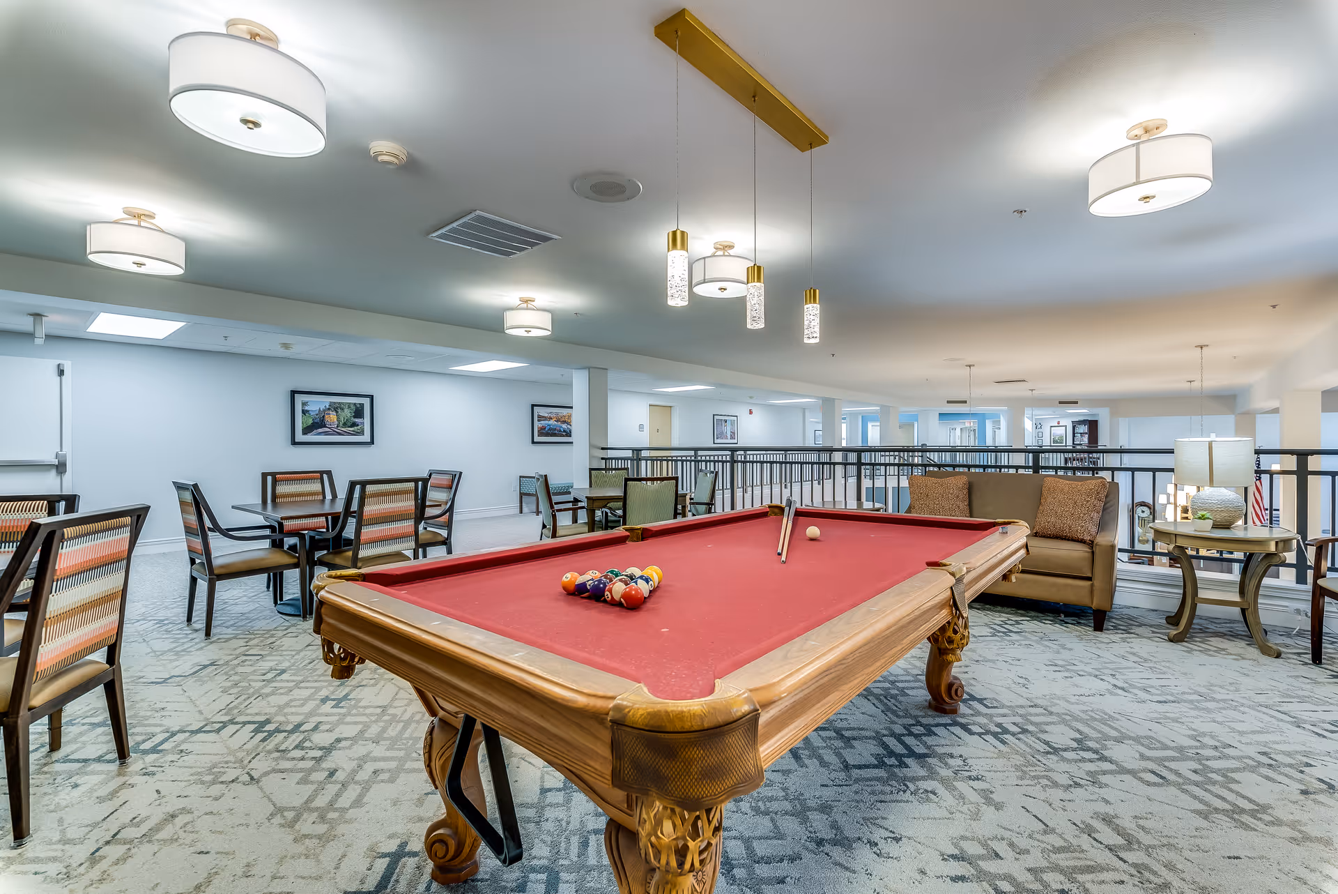 Communal lounge area with a red-felt pool table, seating, and tables under pendant lights.