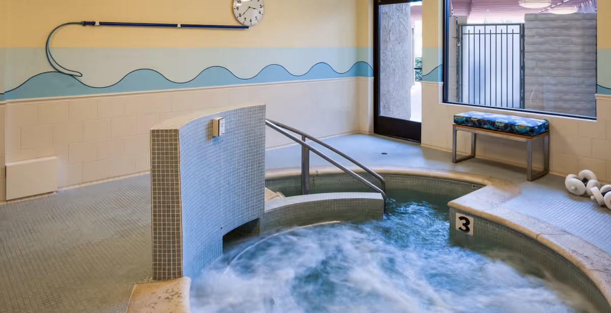 Indoor bubbling whirlpool spa with tiled surround, metal handrail, bench seating and a windowed door.
