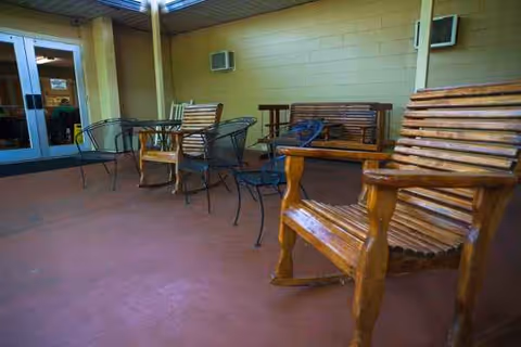 Outdoor patio with wooden and metal chairs and a table near a building entrance.