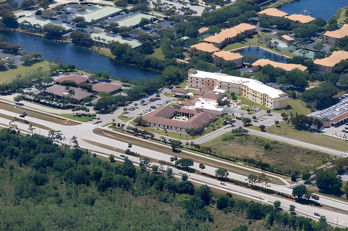 Aerial view of Discovery Commons Cypress Point facility surrounded by greenery, water bodies, and nearby roads with several cars visible.