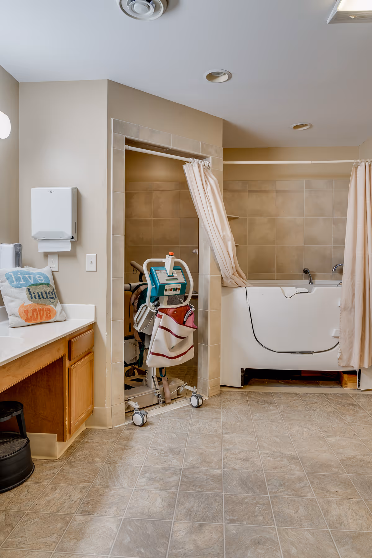 Accessible bathroom with a walk-in tub, privacy curtains, a patient lift, and a vanity countertop.