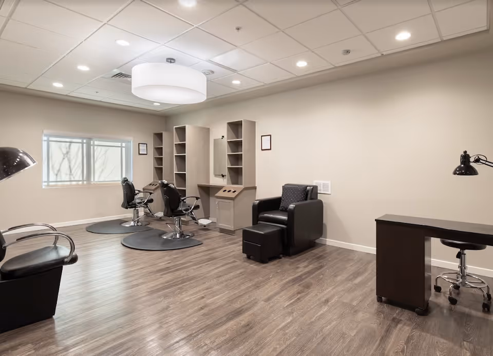 Well-lit salon-style room with styling chairs, shelving, a reclining armchair with ottoman, and a manicure desk.