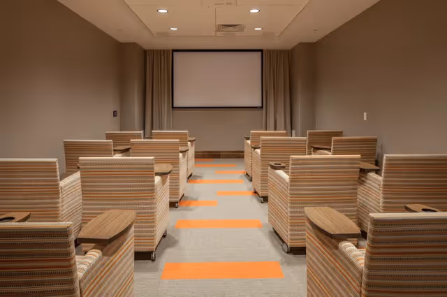 Small screening room with striped upholstered armchairs in rows facing a blank projection screen.