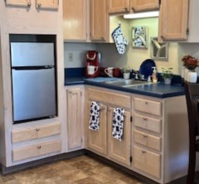 Small kitchenette with light wood cabinets, blue countertop, mini fridge, sink and a red coffee maker