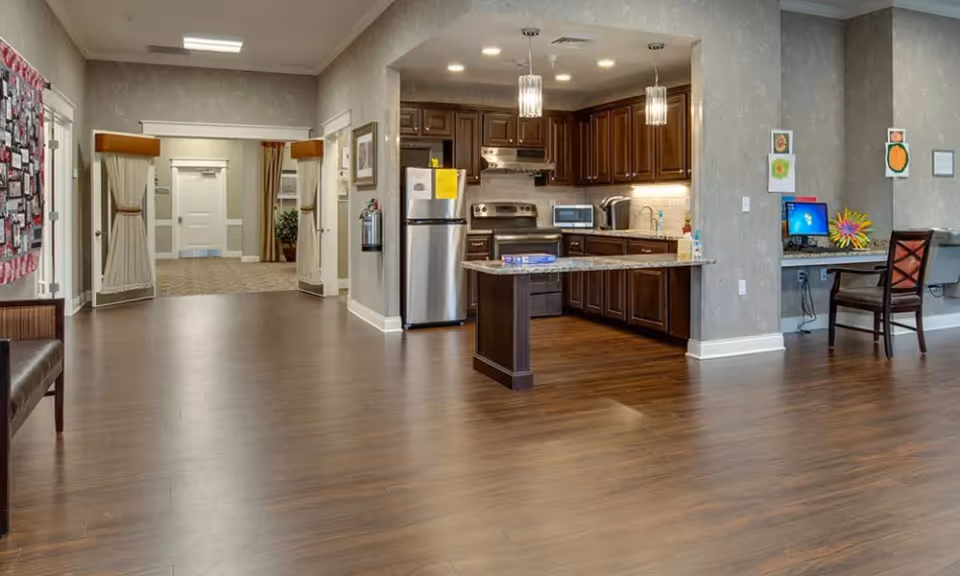 Open communal kitchen and lounge area with a central island, stainless steel appliances, seating and a computer workstation.