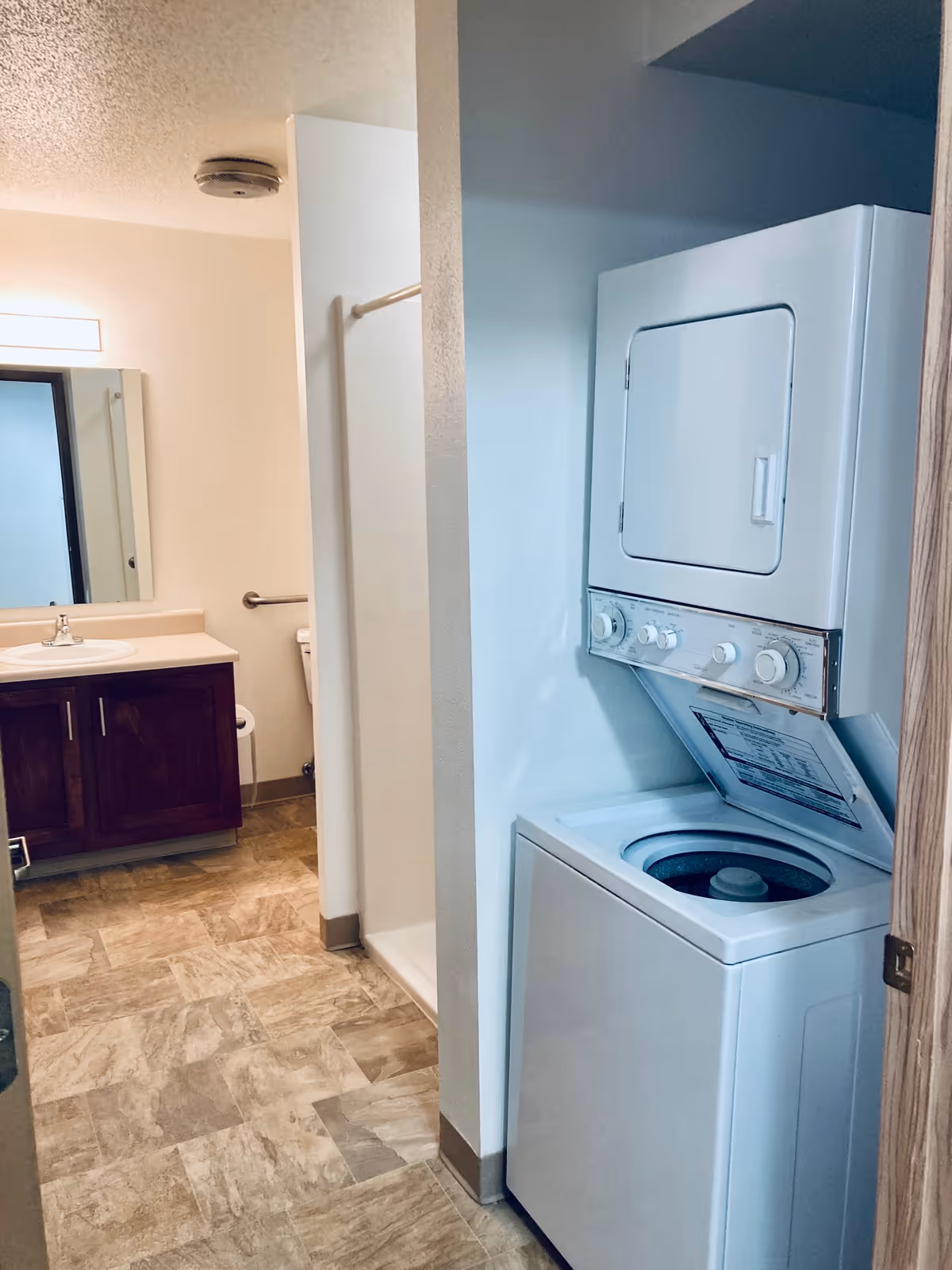 Bathroom interior showing a stacked washer-dryer unit in an alcove, a vanity with sink and mirror, and a shower stall.
