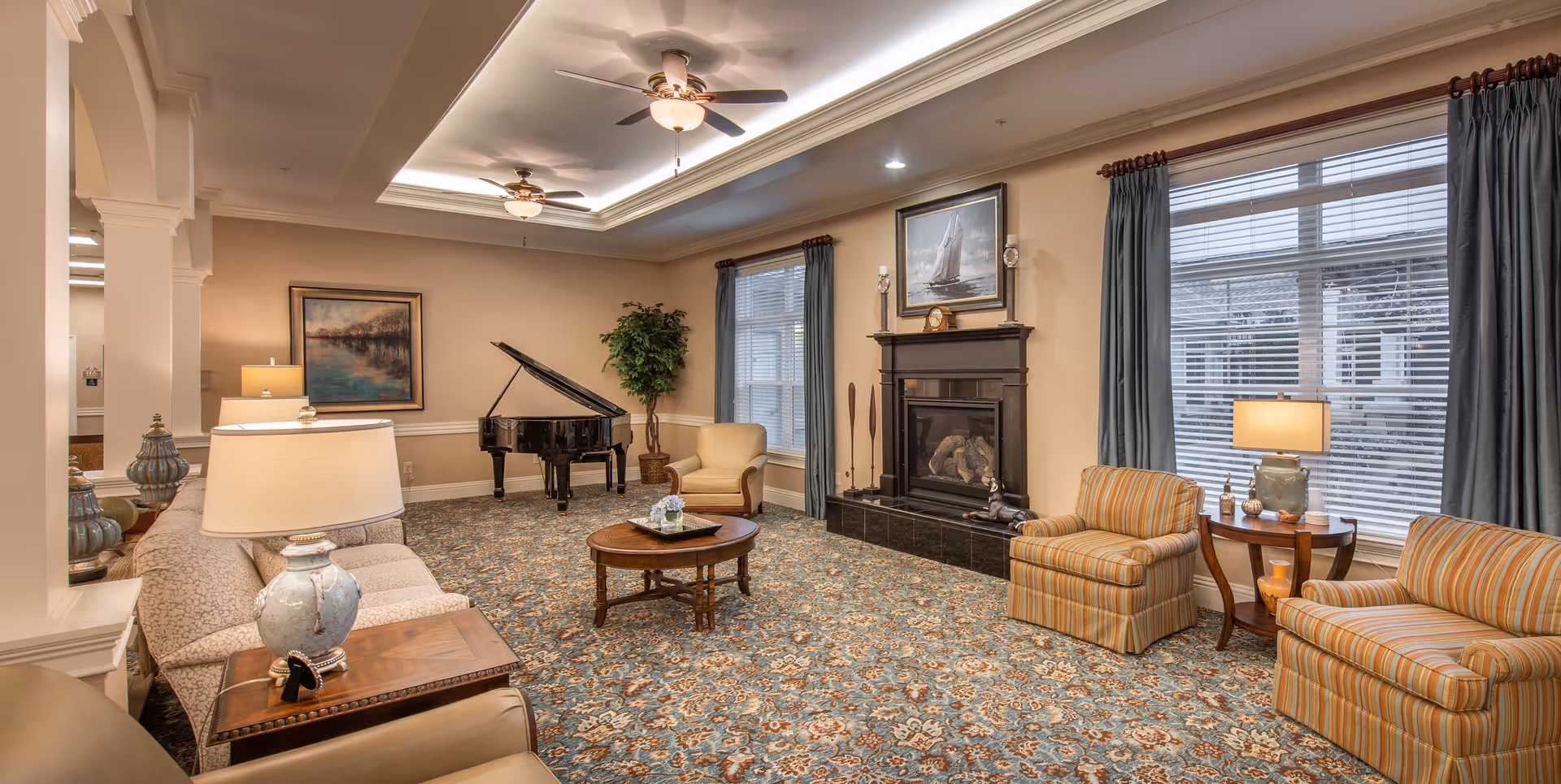 Spacious furnished community living room with sofas and armchairs, a fireplace, grand piano, coffee table, and large windows.