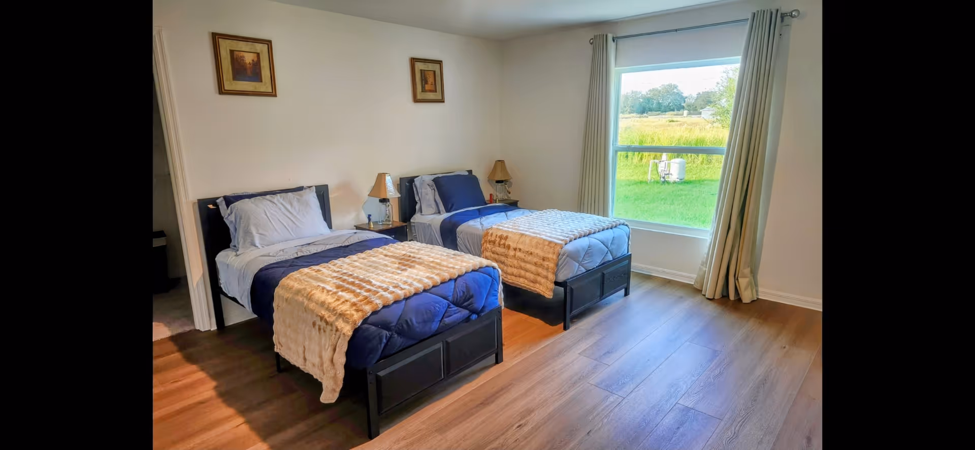 Two twin beds with navy bedding and beige throws in a bright room with a large window and nightstand.