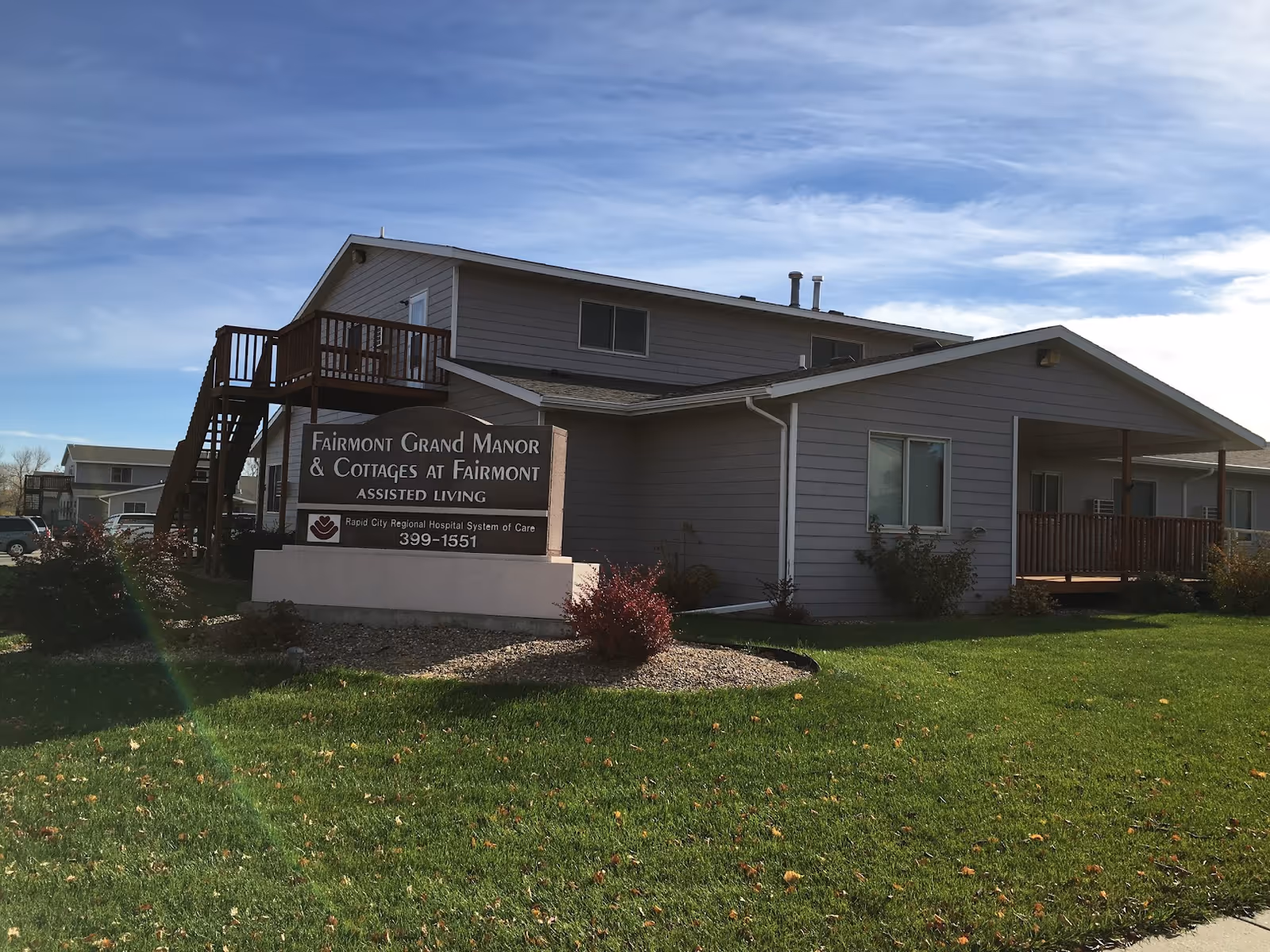 Exterior of Fairmont Grand Manor I with sign, deck, and green lawn.