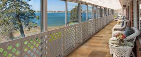 Seaside balcony with wicker chairs along a lattice railing overlooking water.
