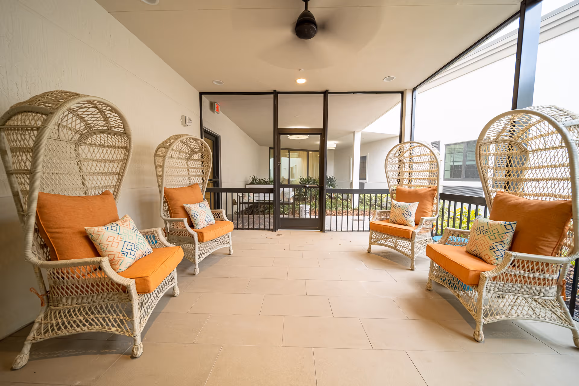 Screened covered patio with four wicker high-back chairs with orange cushions arranged on a tiled floor.
