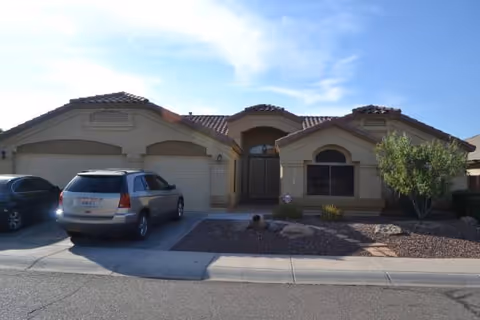 Residential-style building exterior with a driveway, parked SUV, and xeriscaped landscaping.