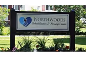 A Northwoods Rehabilitation and Nursing Center sign with a blue heart logo, on a landscaped lawn.