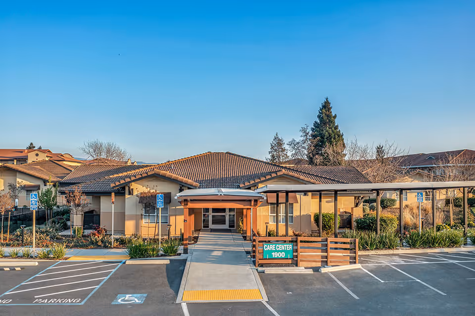 Exterior view of The Meadows of Napa Valley care center building with a covered entrance, accessible parking spaces, and a clear blue sky.