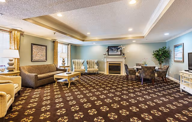 Spacious communal lounge with sofas, armchairs, a fireplace, table seating and patterned carpet under recessed lighting.