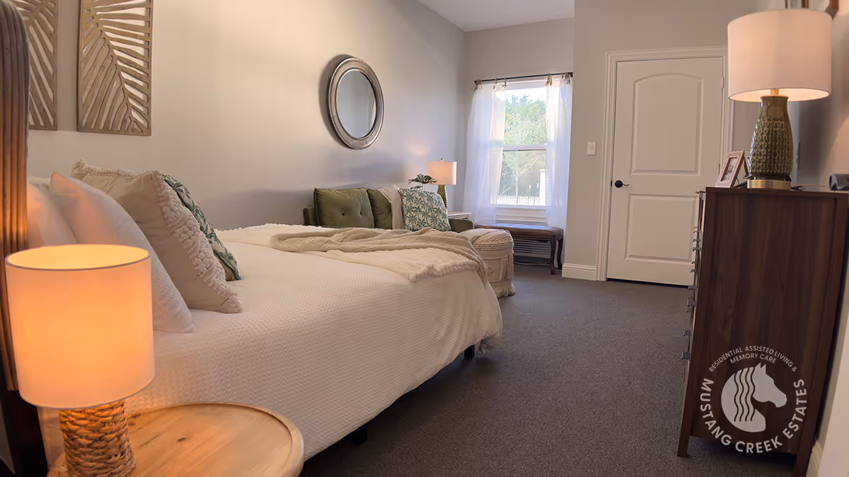 Furnished bedroom with a made bed, bedside lamps, a dresser, and a window letting in natural light.