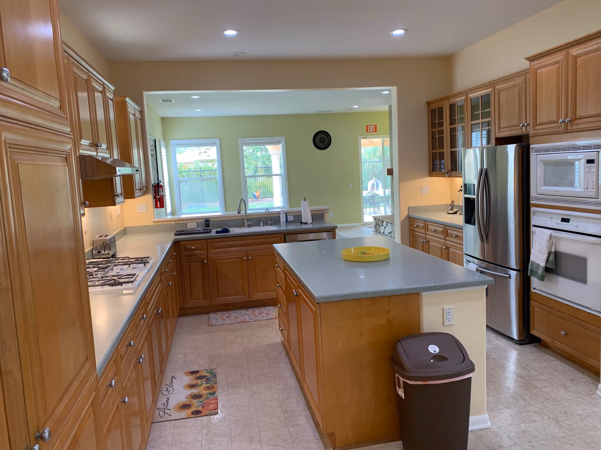 Bright modern kitchen with wooden cabinets, a central island, stainless steel appliances, and windows overlooking a yard.