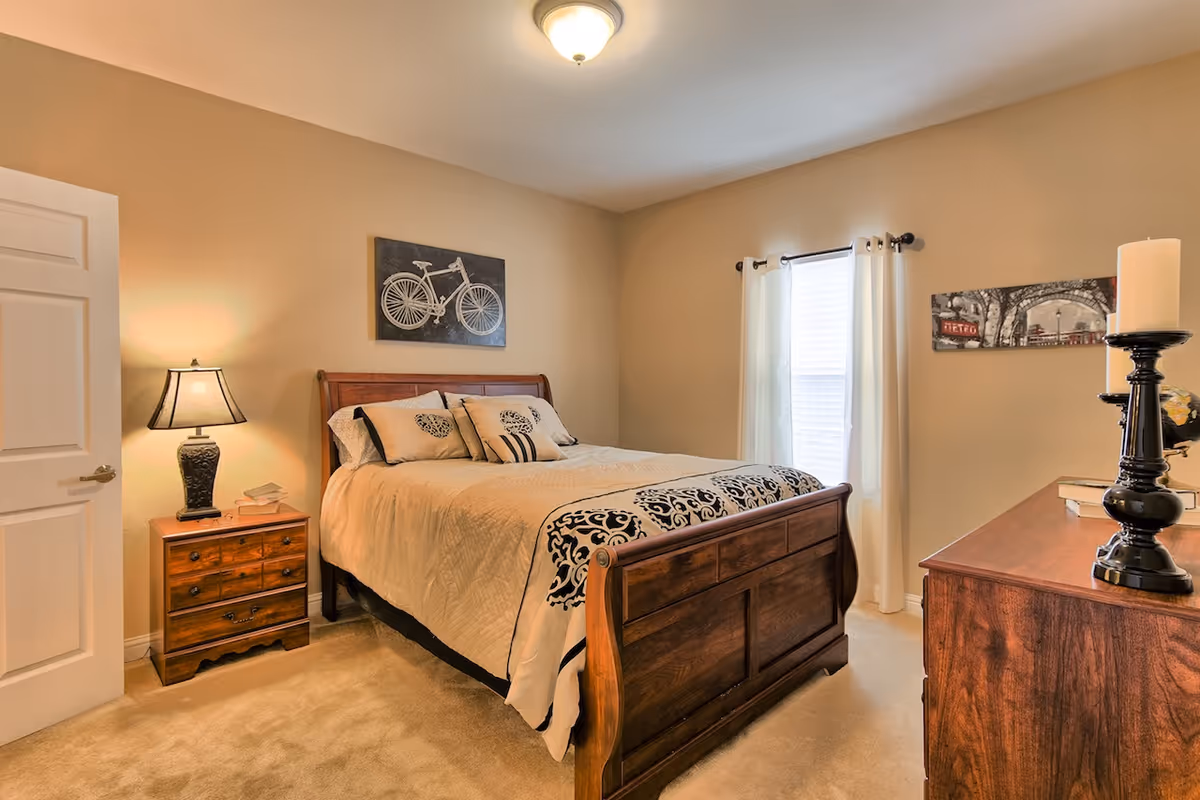 Well-lit bedroom with a wooden bed, nightstand, dresser, and window with curtains.