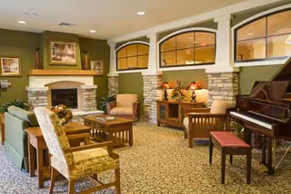Cozy common lounge with fireplace, stone wall, seating, and a piano.
