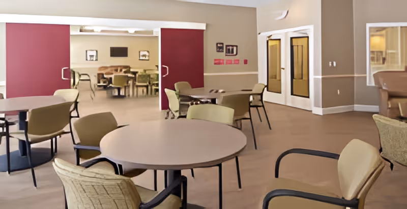 Spacious dining/common room with round tables and chairs, maroon sliding partitions, and double doors.