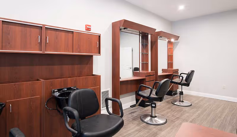 A small salon interior with styling chairs, mirrors, a hair-washing sink, and wooden cabinetry.