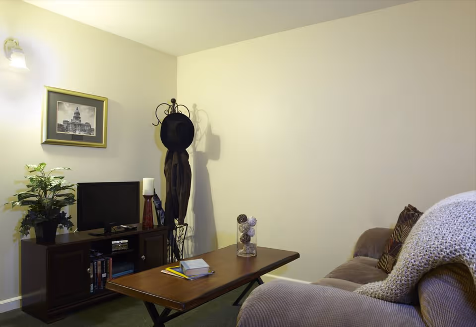 Cozy living room with a sofa and throw, coffee table, TV stand with a small TV, coat rack, plant and framed wall art.