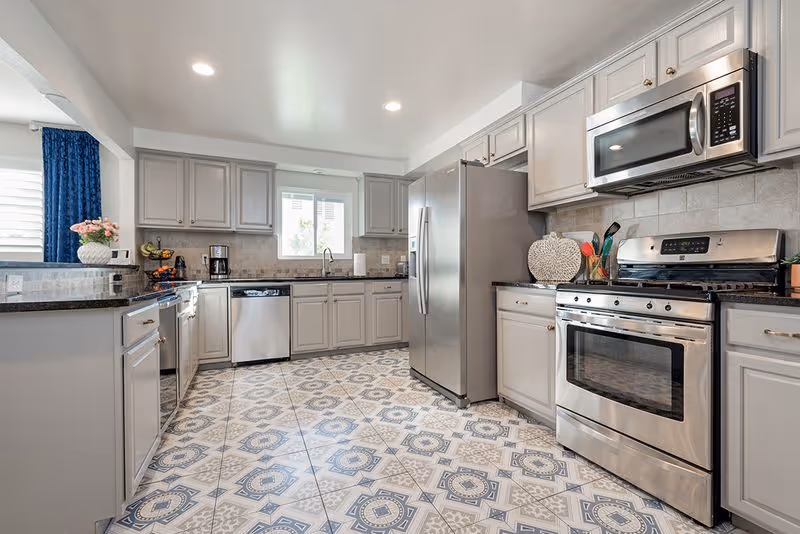 Bright modern kitchen with stainless steel appliances, gray cabinets, black countertops and patterned tile flooring.