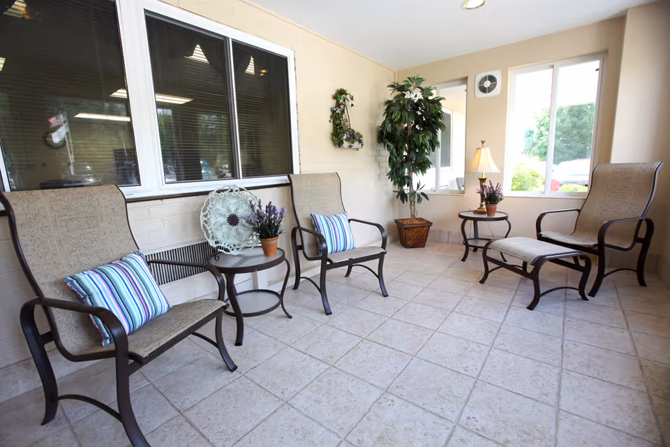 Sunlit seating area with metal-framed lounge chairs, side tables, potted plants, and striped cushions.