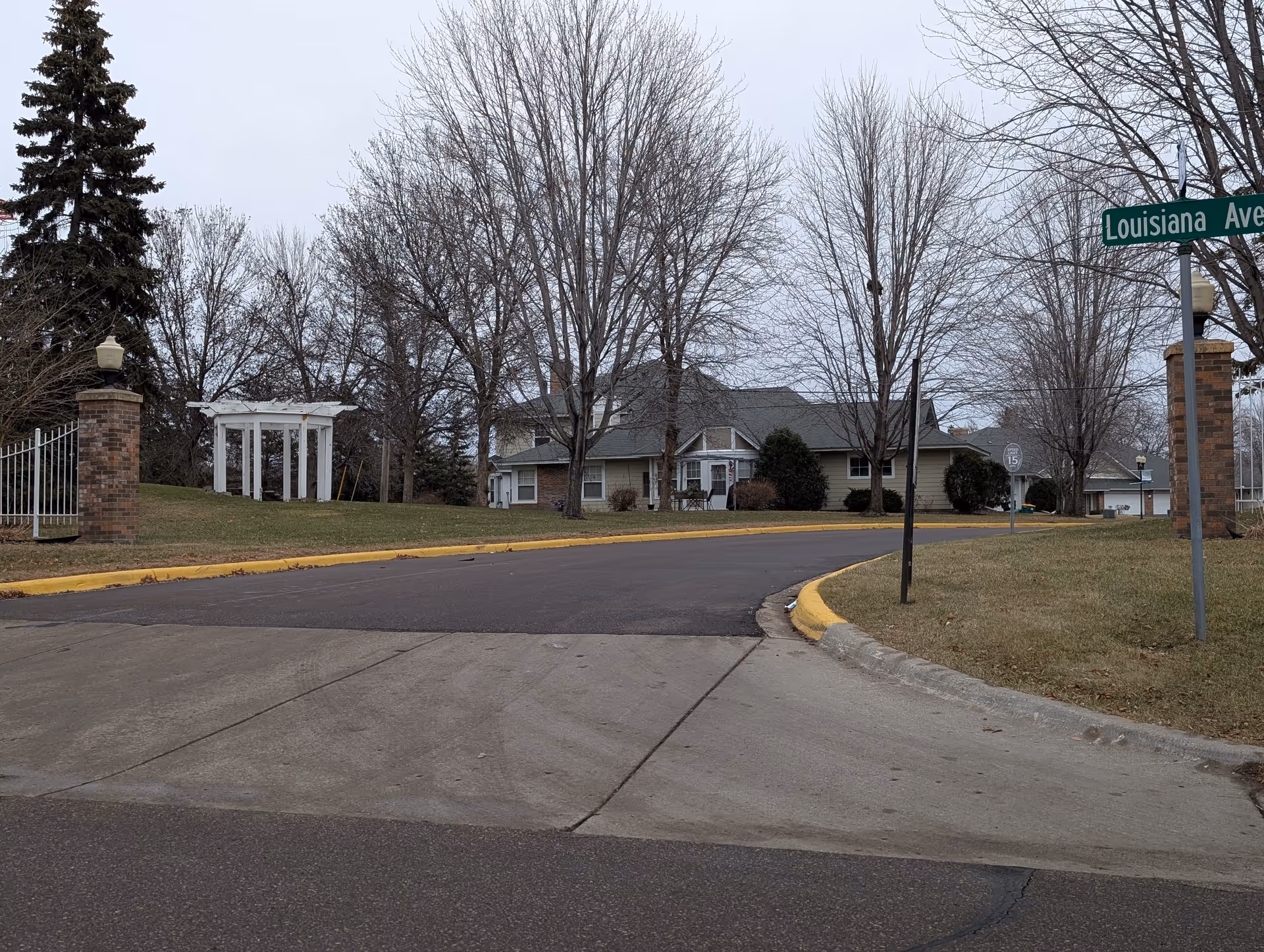 Entrance drive and front exterior of a single-story senior living building among leafless trees with a Louisiana Ave street sign.