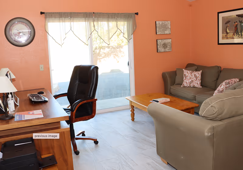 A living room with a desk and office chair, sofas, a coffee table, and a sliding glass door.