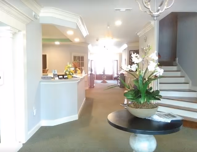 Reception lobby with a round table holding a potted orchid, a front desk on the left, and a staircase on the right.
