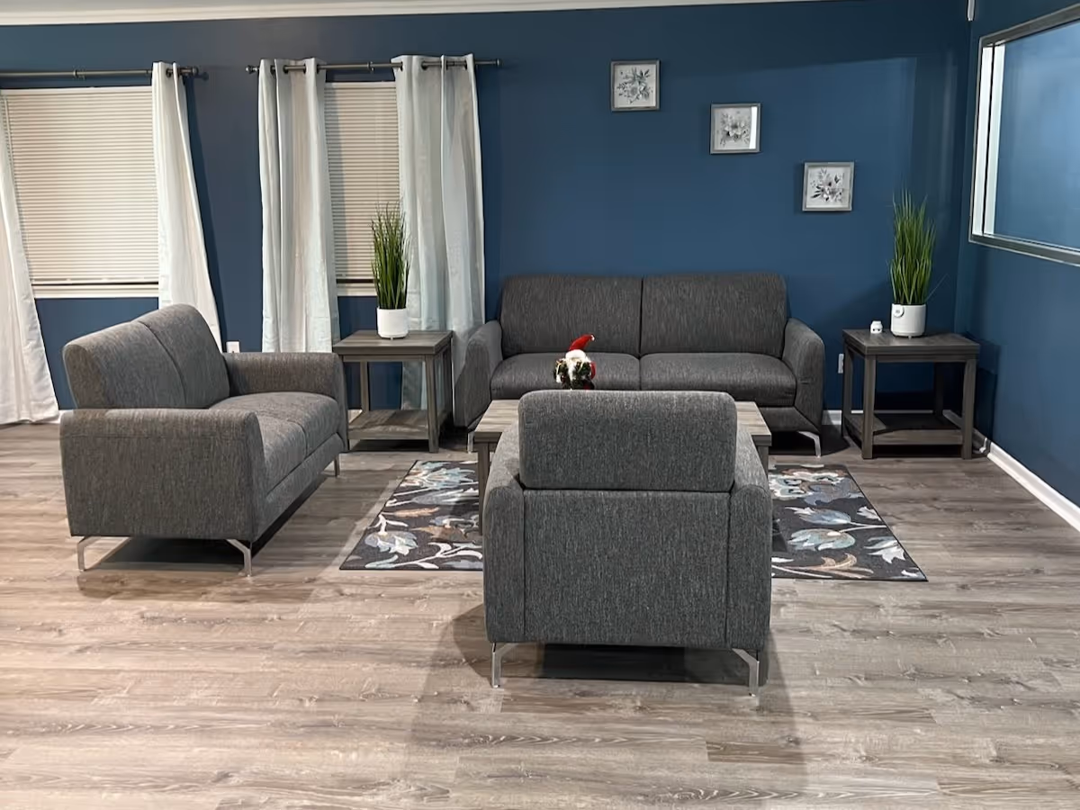 A modern living room with gray sofas and armchairs arranged around a coffee table on a patterned rug against blue walls.