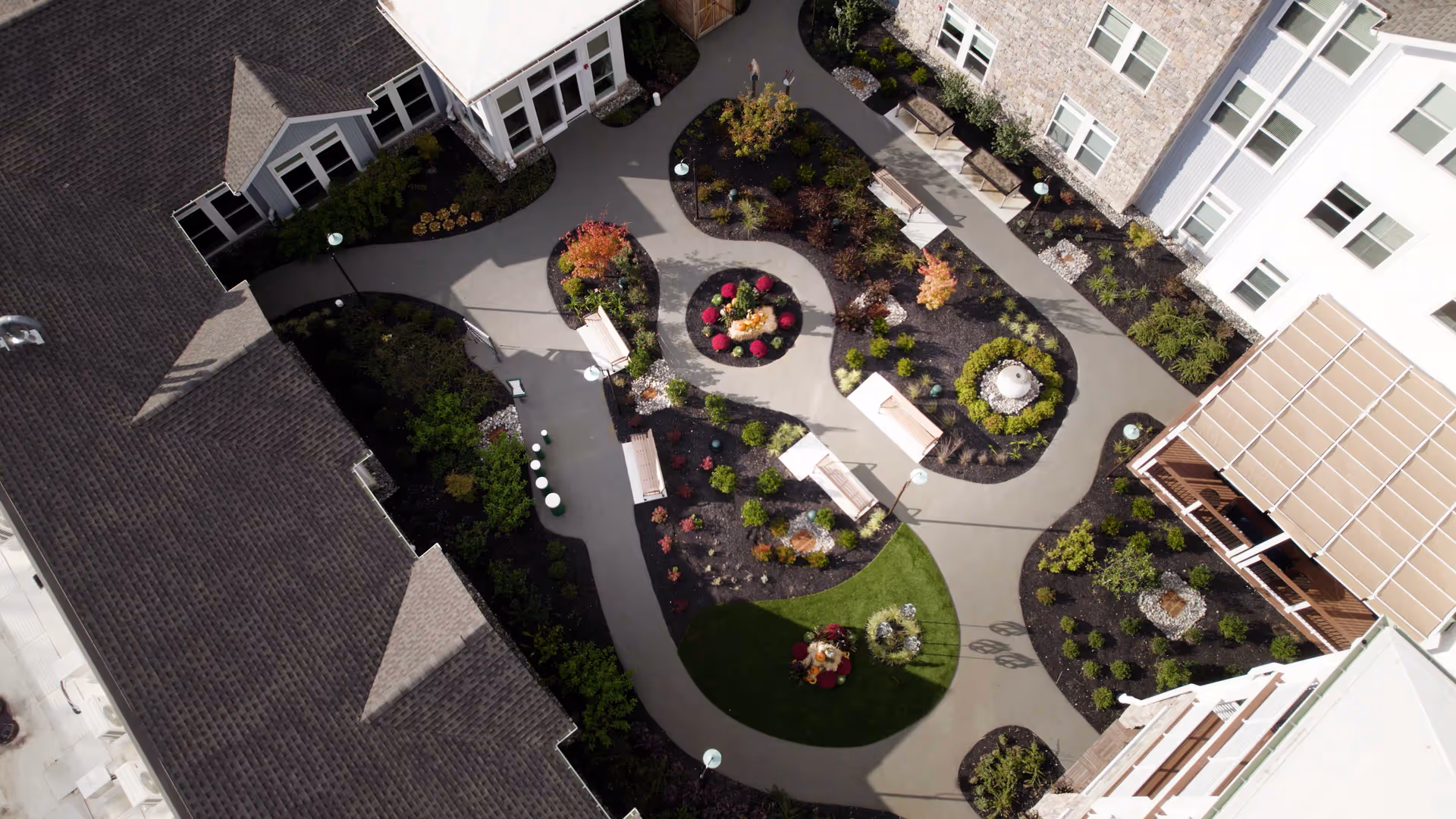 Aerial view of a landscaped central courtyard with winding walkways, benches, planting beds and surrounding senior living buildings.