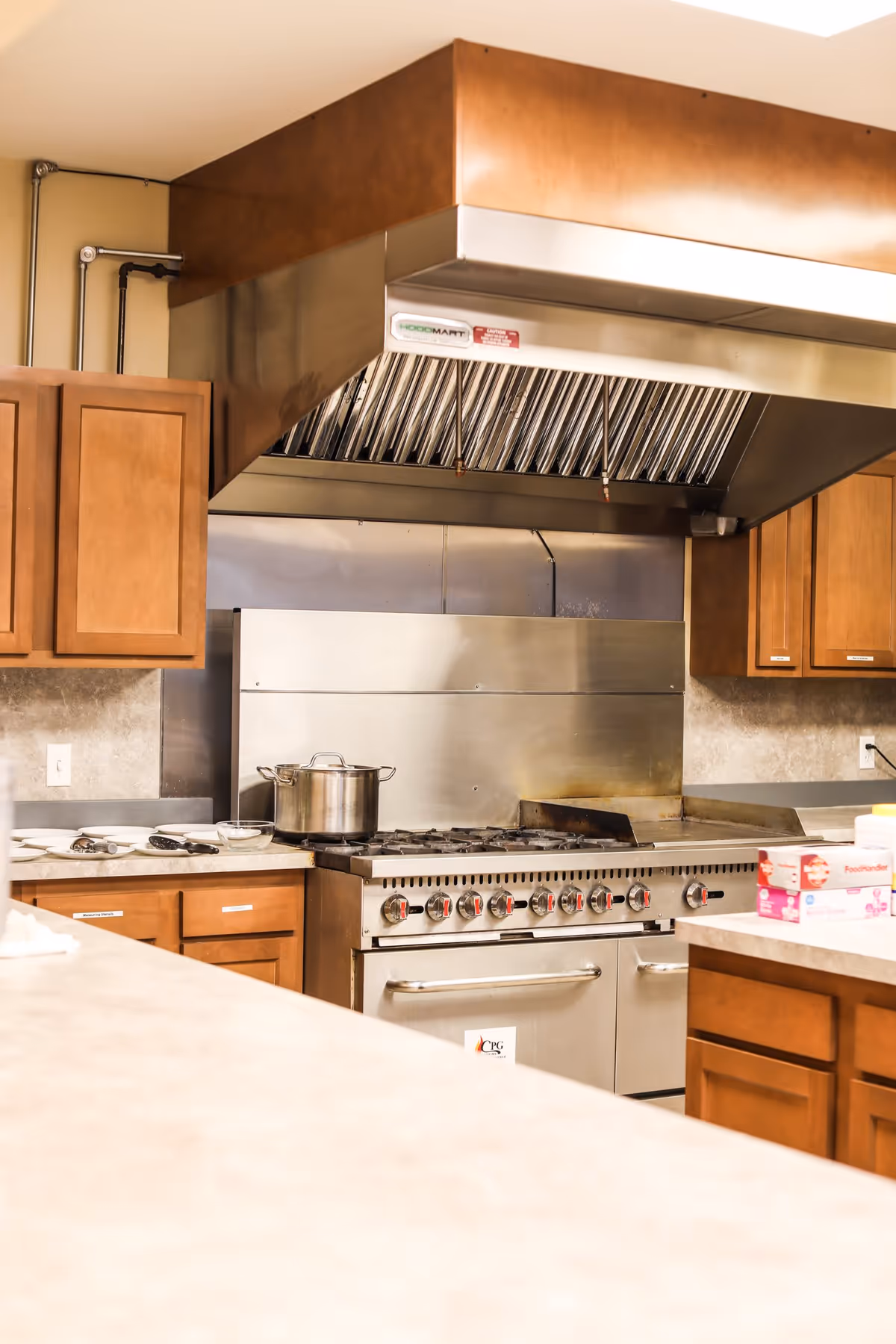 A well-equipped kitchen featuring stainless steel appliances, a large gas stove with multiple burners, and wooden cabinetry. A pot sits on the stove, and various kitchen tools are visible on the countertop.