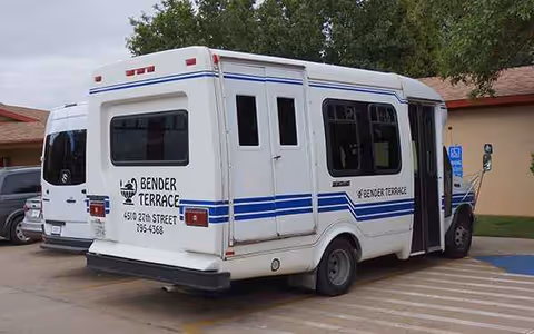 White Bender Terrace bus parked in a lot beside a beige building.