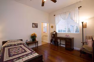A cozy bedroom with a bed, dresser, desk, chair, and a window with curtains.