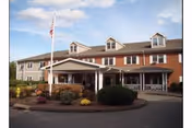 Red brick senior living facility entrance with flagpole, drive circle, and manicured shrubs.