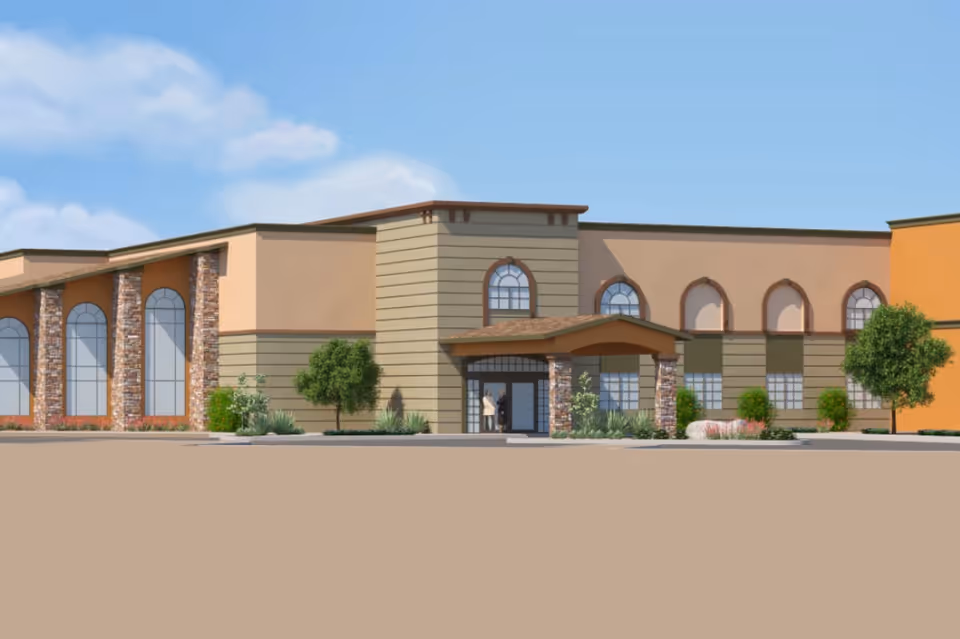 Front exterior view of a two-story senior living facility with arched windows, stone columns, landscaping, and a covered entryway.