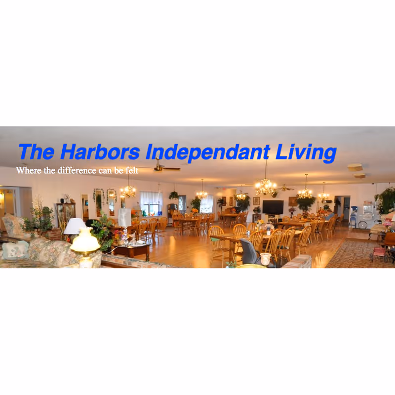 Spacious communal dining and lounge area with many wooden tables and chairs, chandeliers and plants, overlaid with the text 'The Harbors Independant Living'.