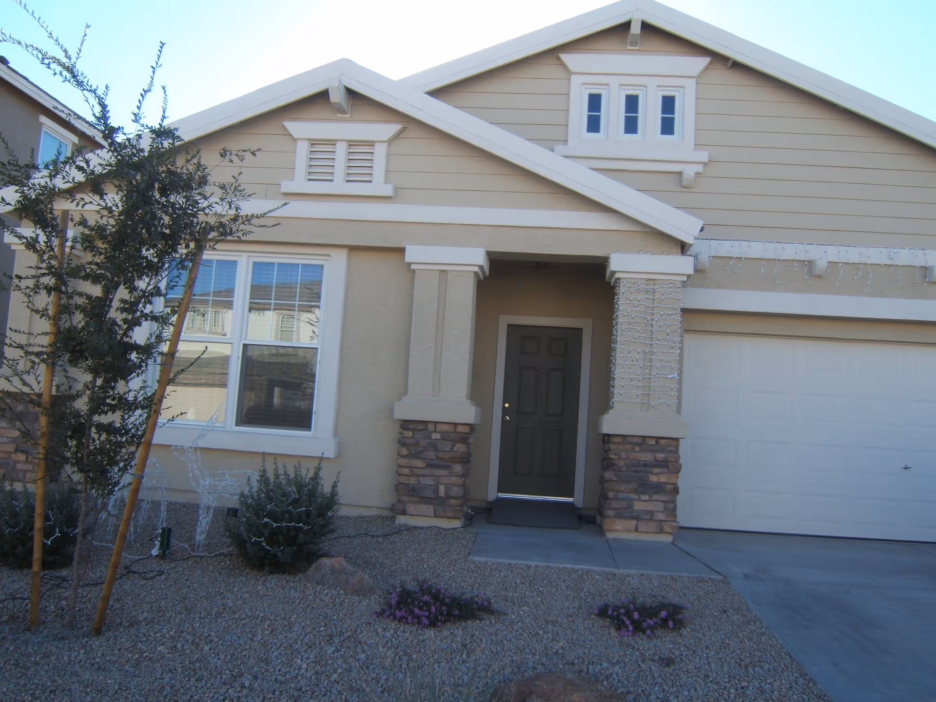Front exterior of a single-family house with a covered entryway, garage door, and gravel landscaping with small plants.