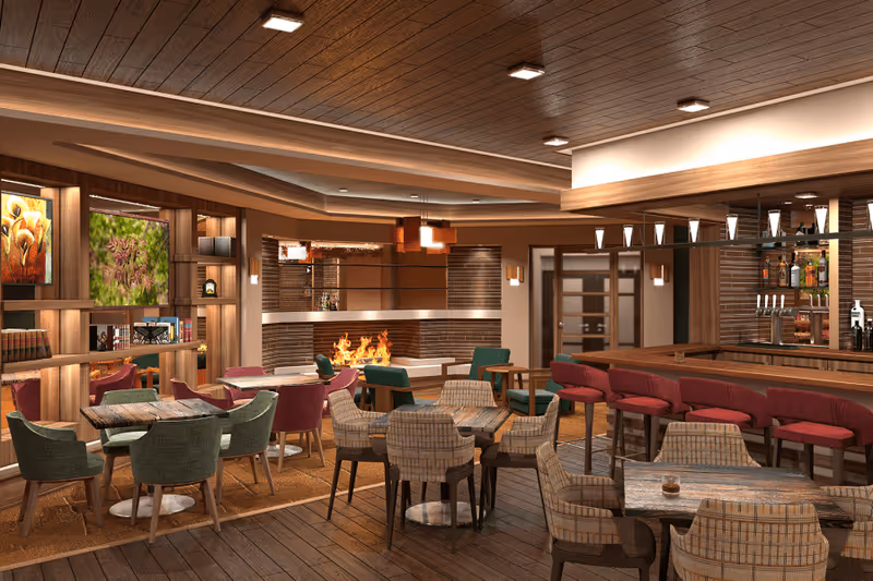 A cozy and modern lounge area with multiple tables and chairs arranged for socializing. The room features a wooden ceiling with recessed lighting, a fireplace with a fire burning, a bar with red cushioned stools, and shelves with books and decorative items. Large windows show greenery outside.