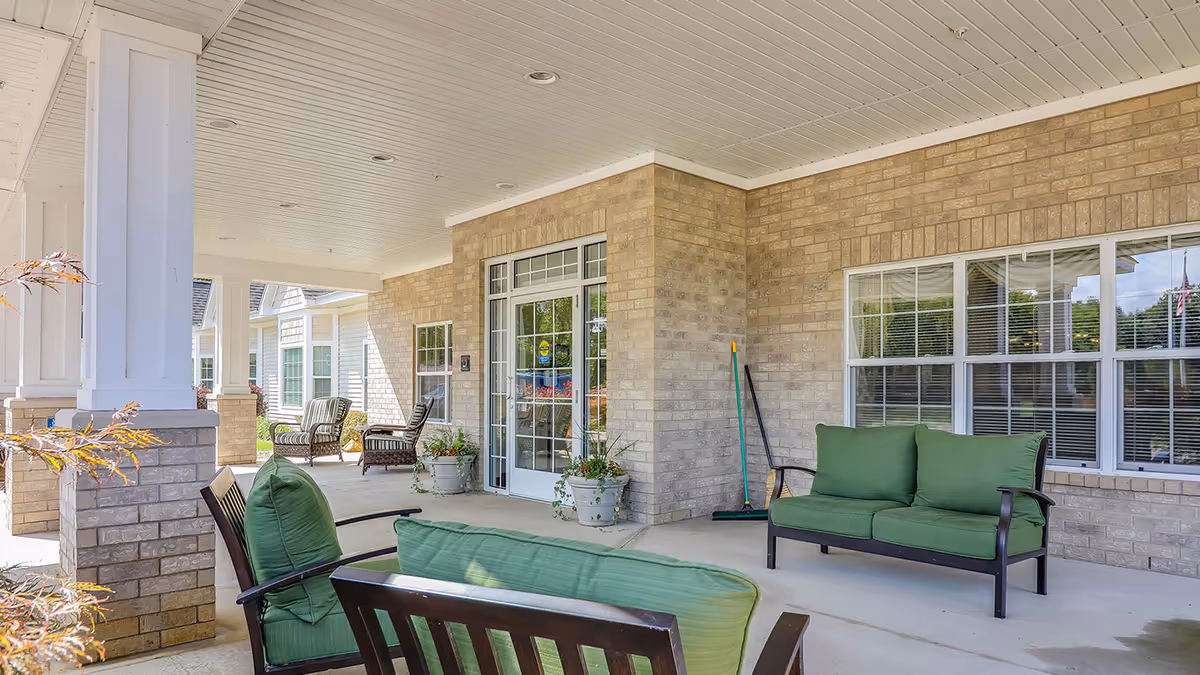 Covered front porch with green-cushioned patio seating, columns, potted plants, and the facility entrance door.