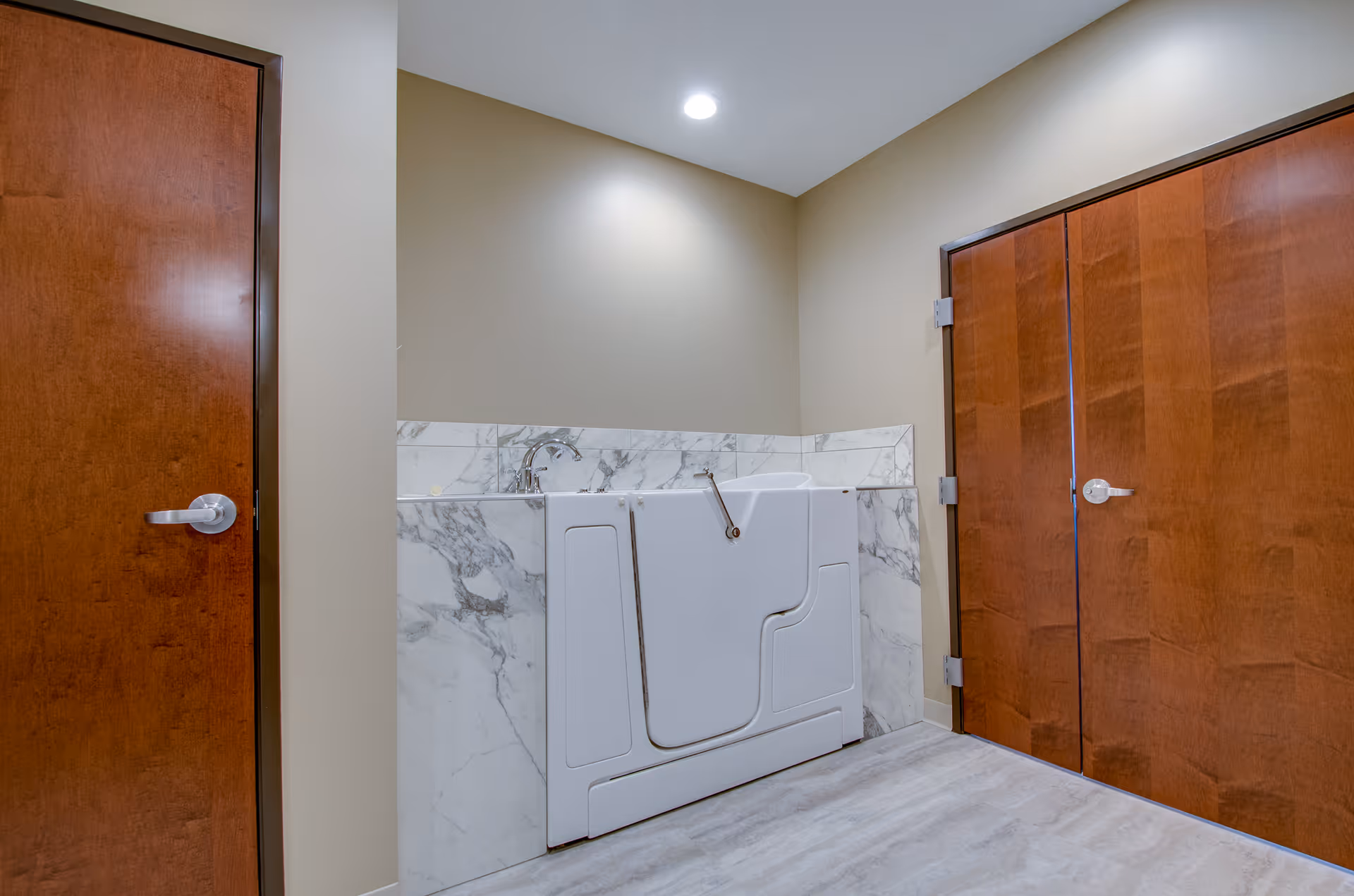 Interior room showing a white walk-in bathtub with a marble surround flanked by two wooden doors.