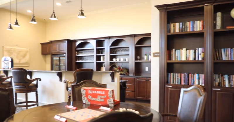 Communal lounge with a round table and Scrabble game, leather chairs, bookshelves and a built-in bar area.