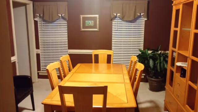A wooden dining table with eight chairs in a dining room, maroon walls, and plants.