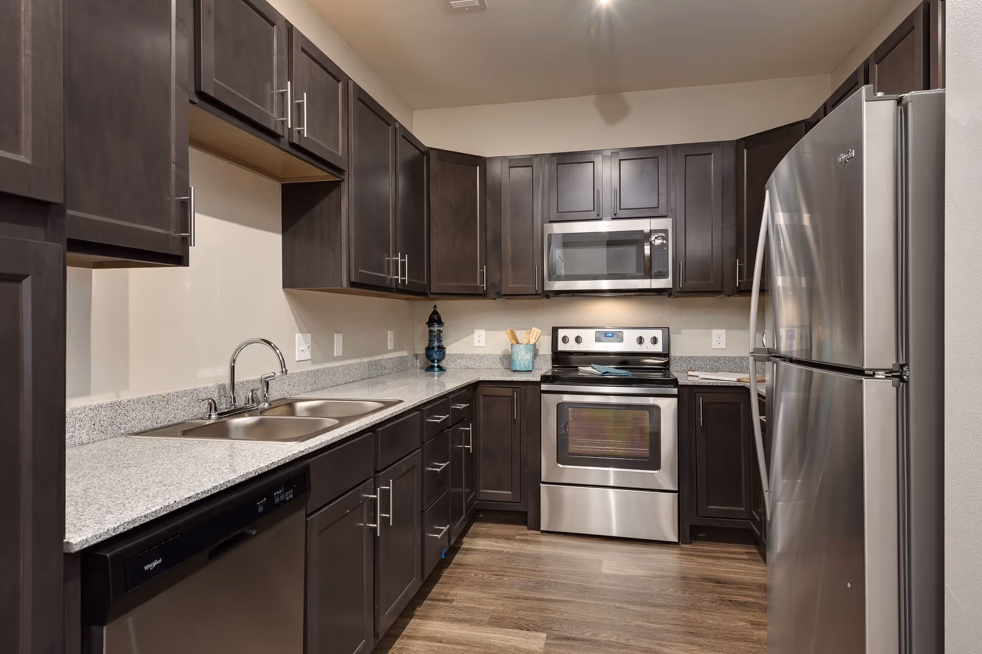 Modern kitchen with dark wood cabinets, granite countertops, stainless steel appliances, and a double sink.